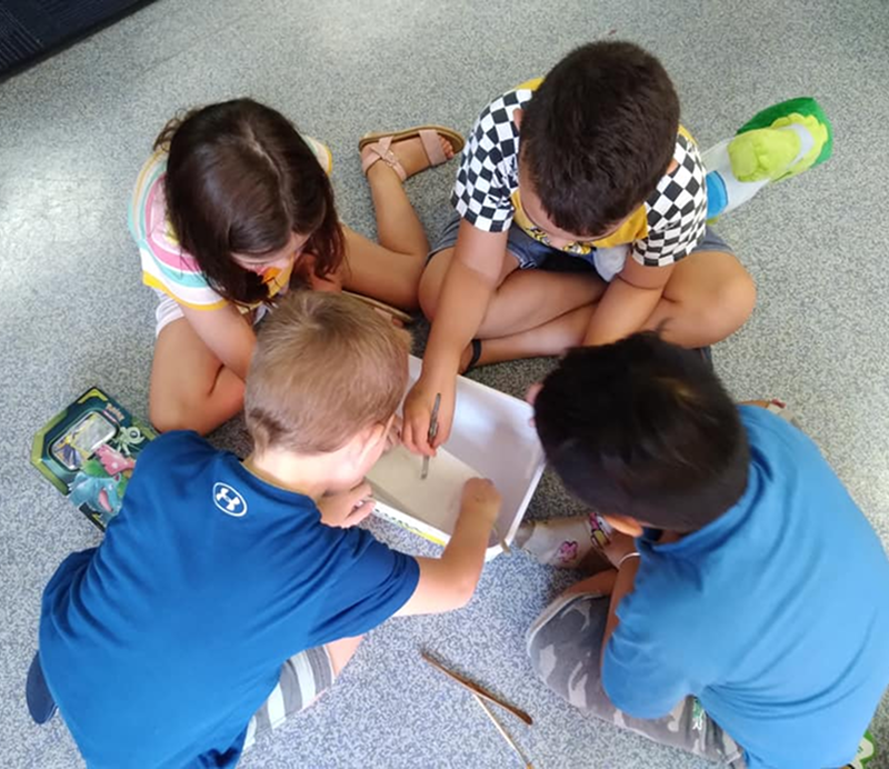 Four children sitting on the floor, engaged with a box, displaying curiosity and excitement.